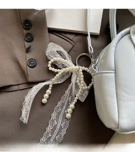 Close-up of pearl bow bag charm with lace ribbon attached to a blue leather handbag
