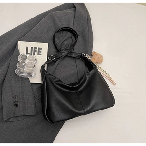 Detail of black matte leather crescent tote bag featuring a cute plush bear charm