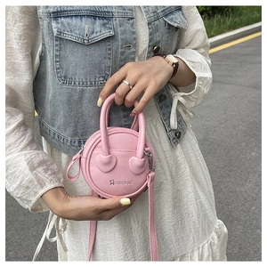 Close-up of pink mini round bag with heart details and litchi texture leather finish