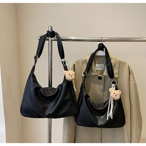 Detail of black PU leather hobo bags with cute teddy bear pendants on a clothing rack
