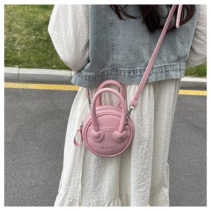 Close-up of pink mini round crossbody bag with heart-shaped handle and litchi texture