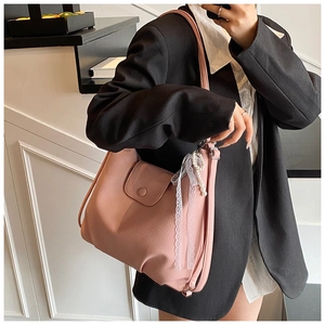 Detalle de bolso rosa en piel sintética con colgante de perlas sobre blazer negro