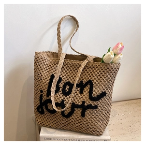 Dettaglio della borsa tote in paglia intrecciata con scritta Bonjour nera e manici intrecciati