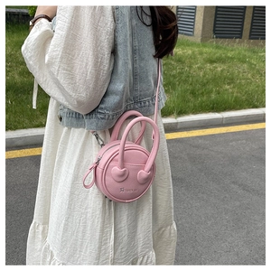 Détail du sac bandoulière rose rond avec attache poignée en cœur et texture cuir grainé