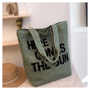 Macro detail of green woven beach tote with Here Comes The Sun embroidery on a wooden shelf