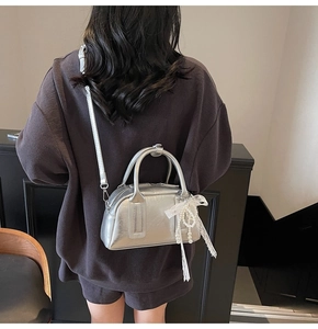 Silver metallic Boston bag with pearl lace bow charm shown on model's back perspective
