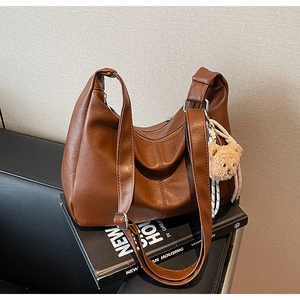 Detail of a large brown faux leather tote bag with an adjustable strap and plush bear charm