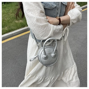Détail d'un petit sac rond argenté avec décoration en forme de cœur sur la bandoulière