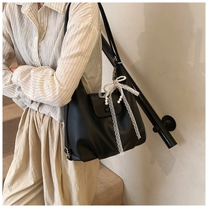 Macro view of black lychee grain leather tote bag with white lace bow and pearl charm