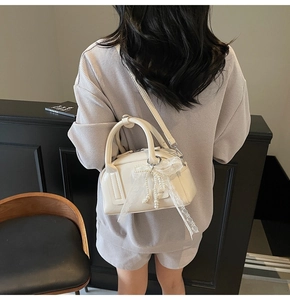 Detail of a creamy white pillow handbag featuring a luxury pearl lace bow charm