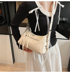 Detalle de bolso de charol blanco roto con cremalleras de flecos largos y ojales plateados