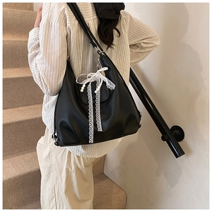 Detalle del bolso tote de cuero negro con elegante lazo de encaje y colgante de perla