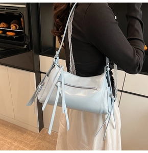 Detalle de bolso hobo de charol azul claro con flecos mostrado en una modelo