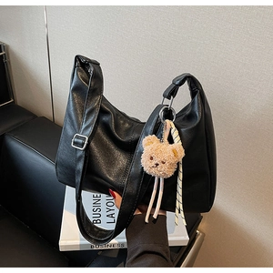 Close-up of black textured leather tote bag with adjustable strap and cute bear charm