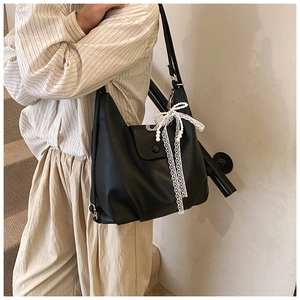 Detalle de bolso tote de cuero negro con encaje blanco y colgante de lazo de perlas