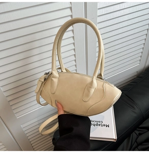 Close-up of a minimalist beige crescent handbag with sleek leather texture and long handles