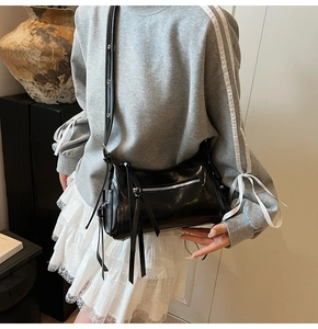 Detalle del bolso bandolera de charol negro con flecos largos y cremallera metálica