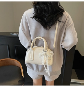 Detail of off-white glossy pillow bag featuring a delicate lace bow and adjustable strap