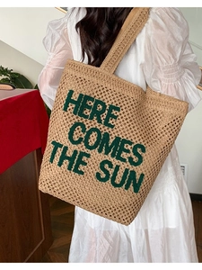 Straw woven tote bag with green embroidery Here Comes The Sun held by a model