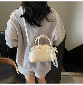 Rear view of model holding cream Boston bag with delicate lace bow and pearl charm