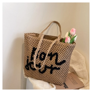 Dettaglio della borsa tote in paglia intrecciata a mano con ricamo Bon Jour e manici