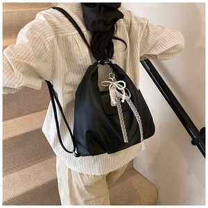 Detail of black faux leather tote with pearl and lace bow charm on indoor stairs