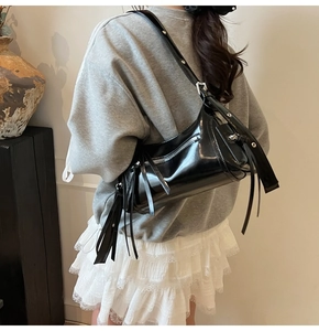 Detalle del bolso de hombro negro brillante con flecos y tachuelas metálicas en la correa