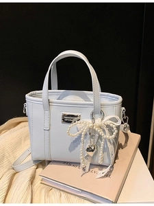 Minimalistische hellblaue Beuteltasche mit Perlenbogen und Herzanhänger auf dunklem Grund
