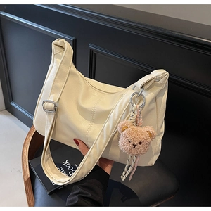 Detail of off-white faux leather tote bag with wide strap and plush bear charm