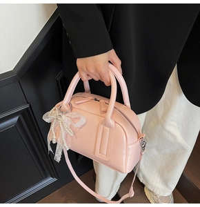 Pink Boston handbag with glossy finish and pearl lace bow charm detail shown on hand
