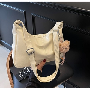 Detail view of cream white PU leather tote with plush bear charm and metal buckle