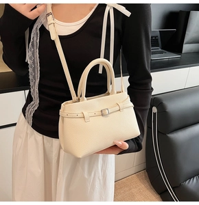 Close-up of cream white lychee texture bucket bag with metal buckle on a black sofa