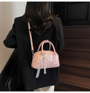 Detail of pink faux leather handbag featuring lace and pearl bow charms on a dark background