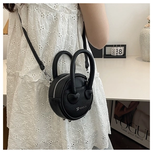 Detail of black crossbody bag with star logo and face pattern on a white lace dress