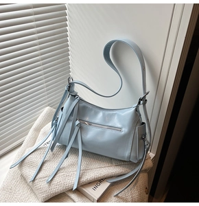 Detalle del bolso de hombro azul claro con flecos sobre tela de tweed y luz suave