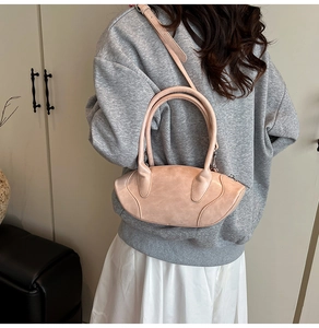 Detail of a dusty pink leather semi-circular handbag worn over the shoulder by a model