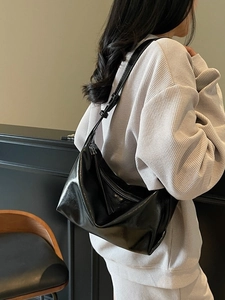 Fashionable black glossy crossbody dumpling bag with adjustable strap shown on model