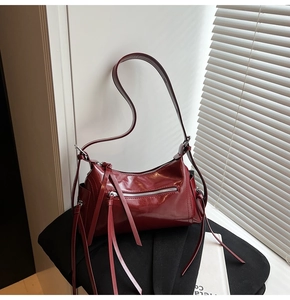 Detalle de bolso burdeos de piel brillante con borla decorativa y herrajes plateados