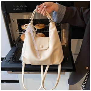 Detalle de bolso tote beige con textura de lichi, lazo de encaje y dije de perla