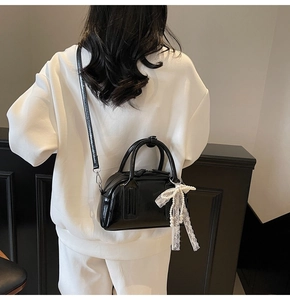 Glossy black patent leather Boston bag with decorative lace bow and pearl charm detailing