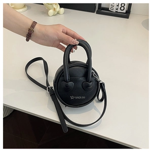 Détail d'un mini sac à main noir rond avec motif de cœur et bandoulière amovible