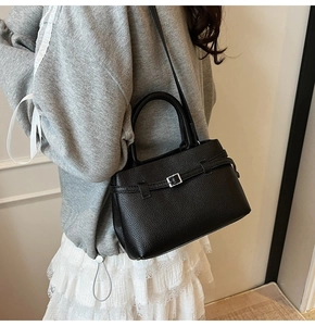 Close-up of black lychee-textured bucket bag with dual handles shown on a model