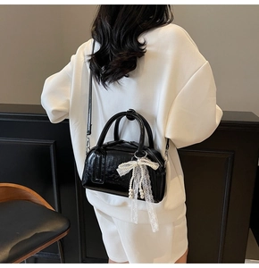 Detail of glossy black crossbody bag with decorative lace bow and white pearl charms