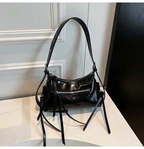 Primer plano del bolso de hombro negro brillante con cremalleras y borlas largas