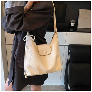 Detail of beige textured leather tote bag featuring pearl bow and lace ribbon charm