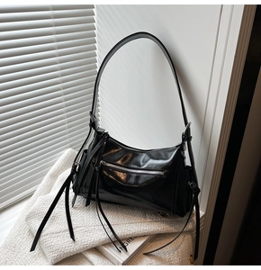 Detalle de bolso de hombro en charol negro con cremalleras metálicas y flecos