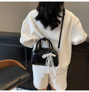 Detail of glossy black Boston bag with lace bow and pearl chain on white outfit