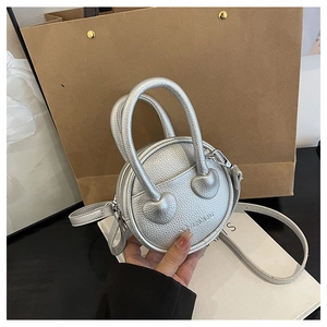 Détail du sac à main rond argenté avec texture litchi et fixations en forme de cœur