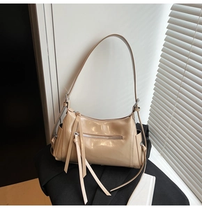 Detalle de bolso de hombro en charol beige con borla decorativa y herrajes plateados