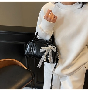 Detail of black glossy Boston bag featuring a large white lace bow with pearl pendant
